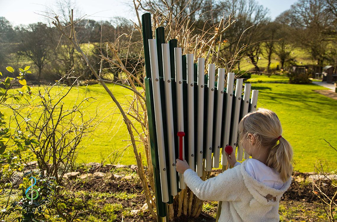 Young girl playing large vertical xylophone in the countryside