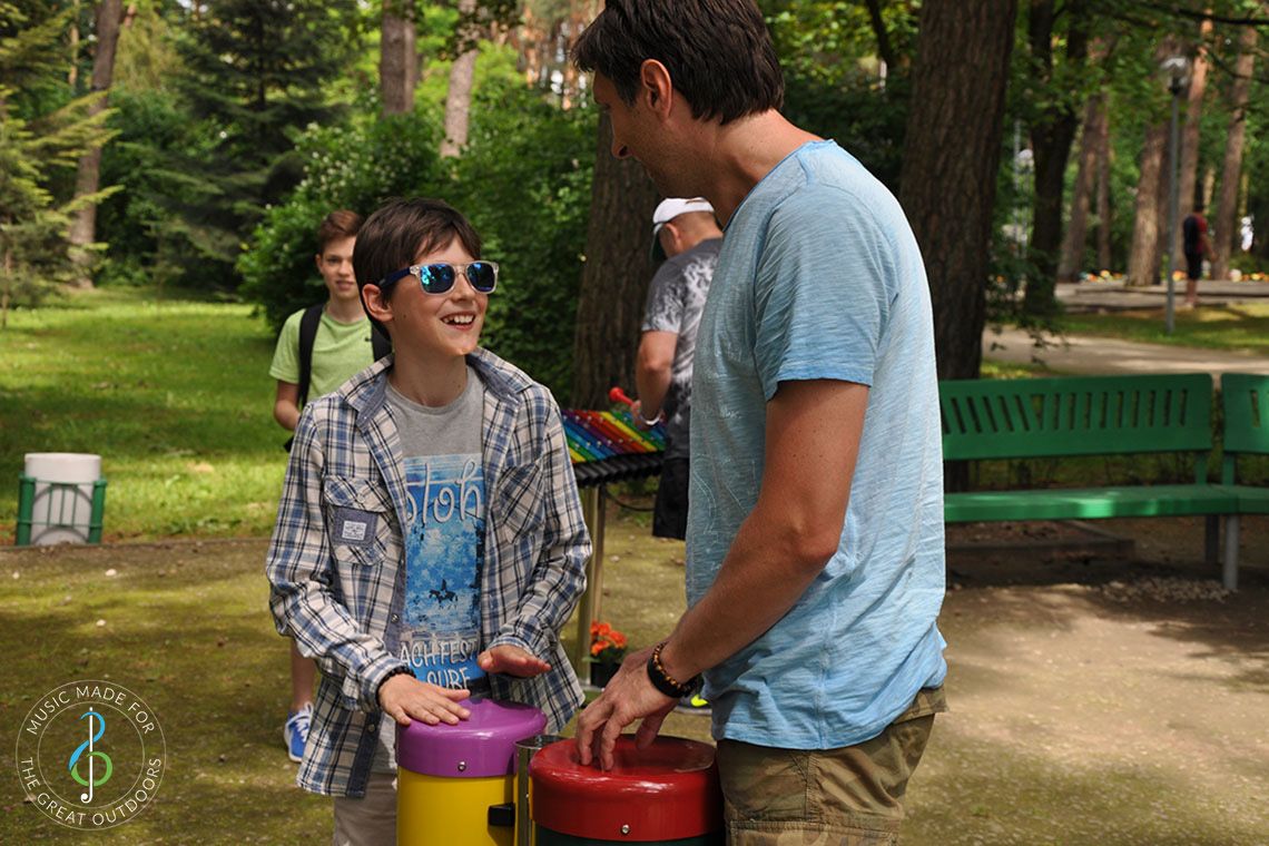Teenage Boy wearing sunglasses with his father playing outdoor conga drums in playground with musical instruments
