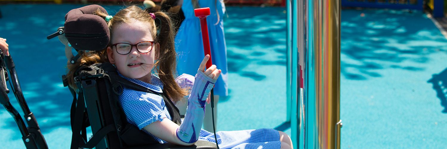 Little girl in a wheelchair playing an outdoor musical instrument in her school playground