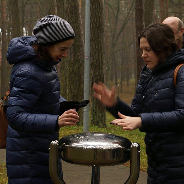 Two ladies playing a stainless steel tongue drum in a city park