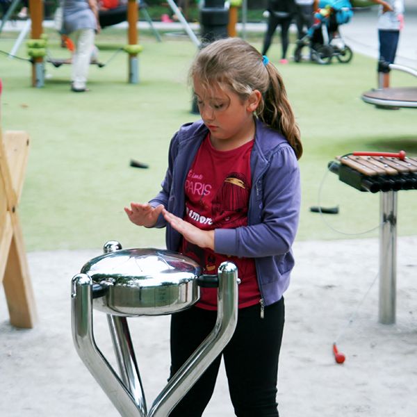 girl playing a round stainless steel tongue drum in a busy park
