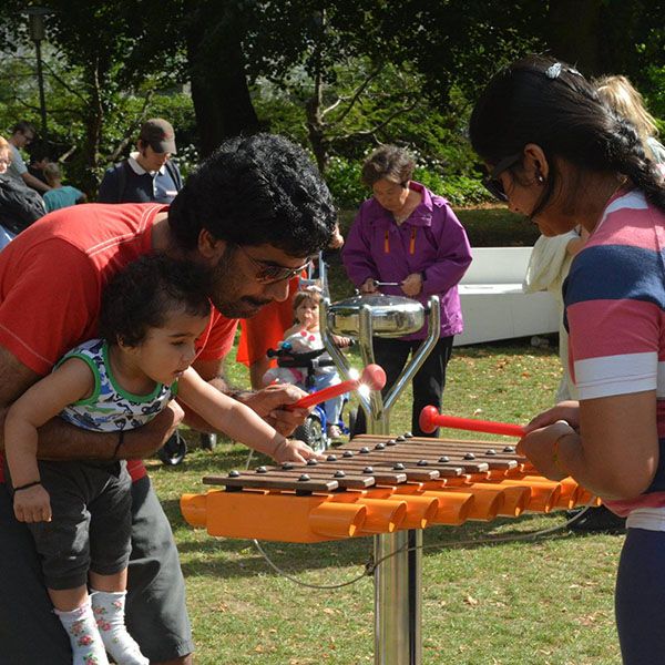 Parents with Father holding a baby playing an orange xylophone in a park