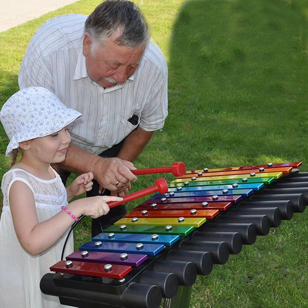 Rainbow Coloured Outdoor Xylophone in Park being played by a small girl with her grandad watching