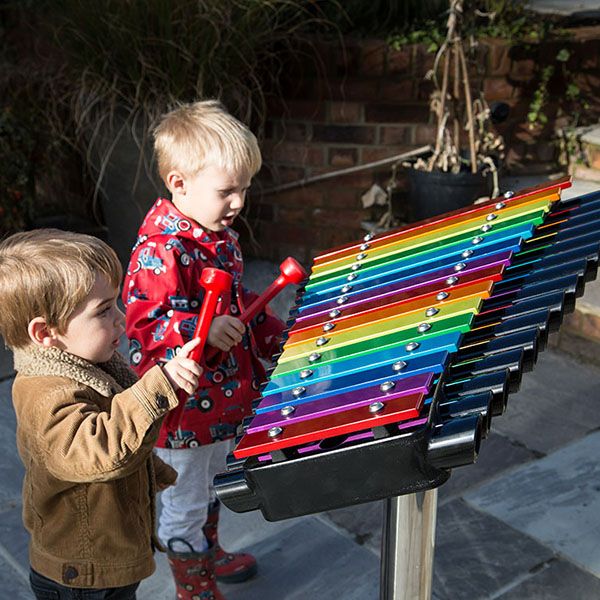 two little boys playing a large rainbow coloured xylophone in a playground