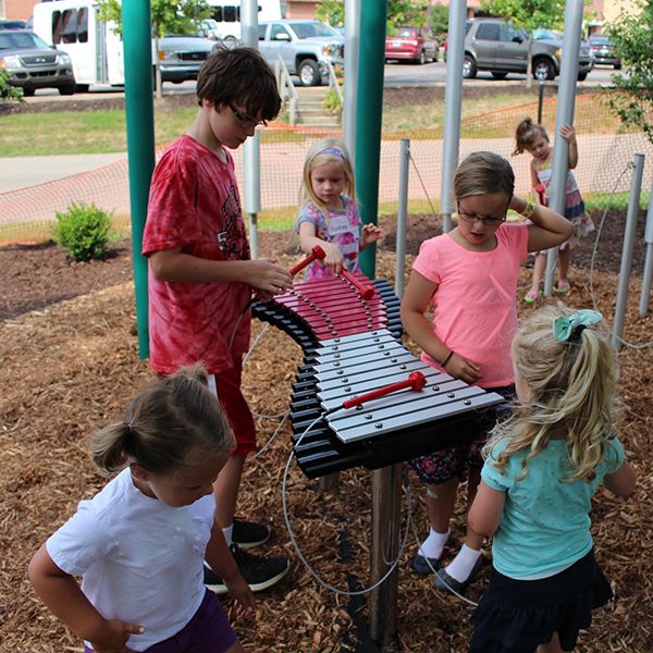 Group of children gathered around a large outdoor xylophone in school yard