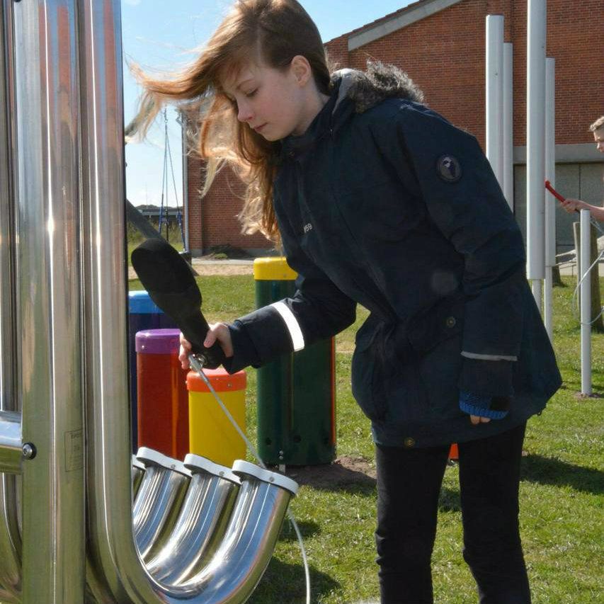 girl hitting large silver outdoor aerophones or slap tubes in school playground
