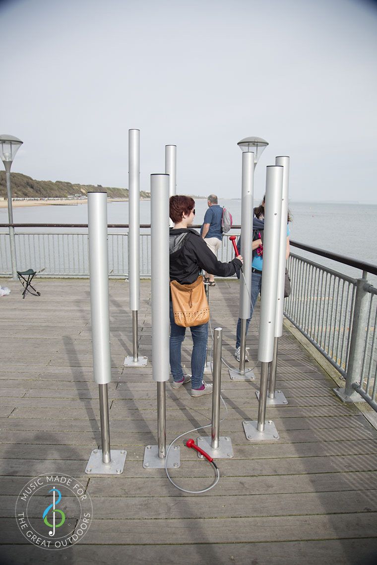 woman playing large upright silver musical chimes on end of pier