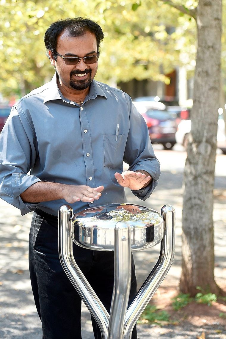 man in a park playing a large metal outdoor tongue drum