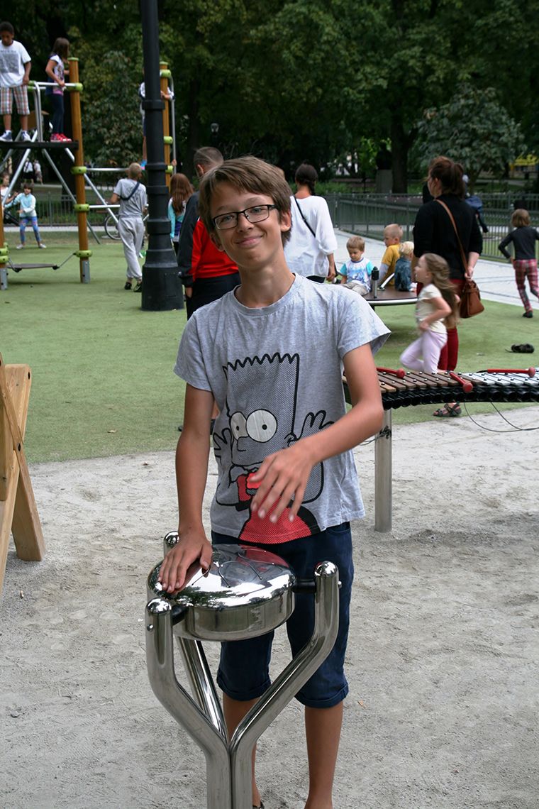 young man playing a stainless steel tongue drum in a busy playground