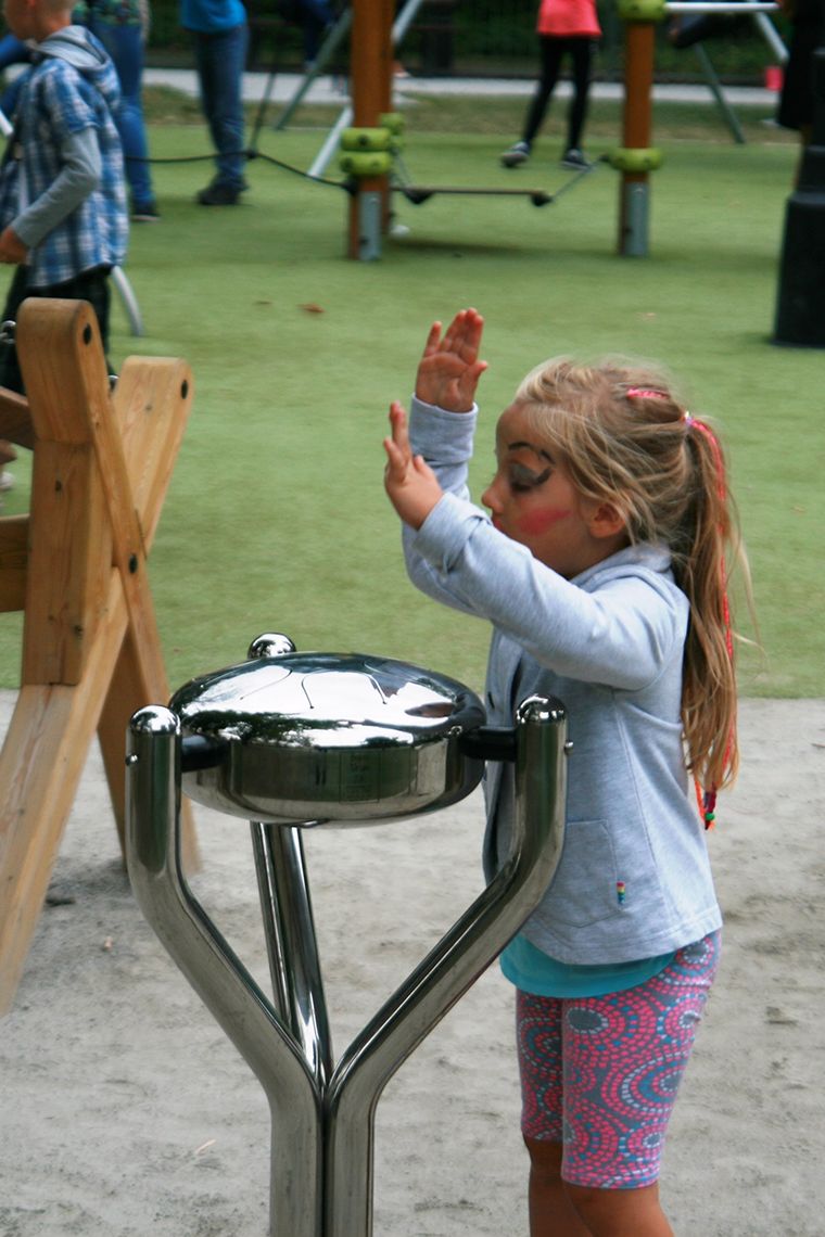 Young girl playing a silver steel tongue drum in a playground