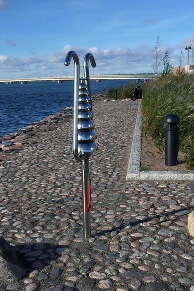 Image of a Percussion Play Bell Lyre - a large outdoor bell tree made of stainless steel - beside a river in Finland