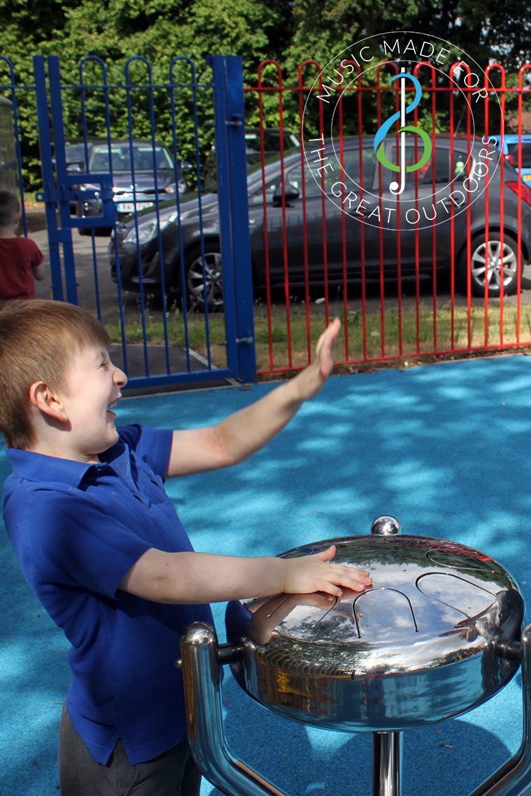 boy playing silver tongue drum in a school playground