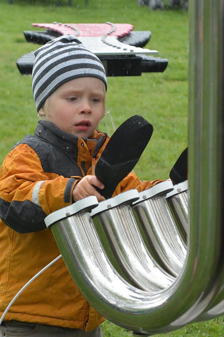 Little boy wearing a winter hat playing a large silver musical instrument in a park
