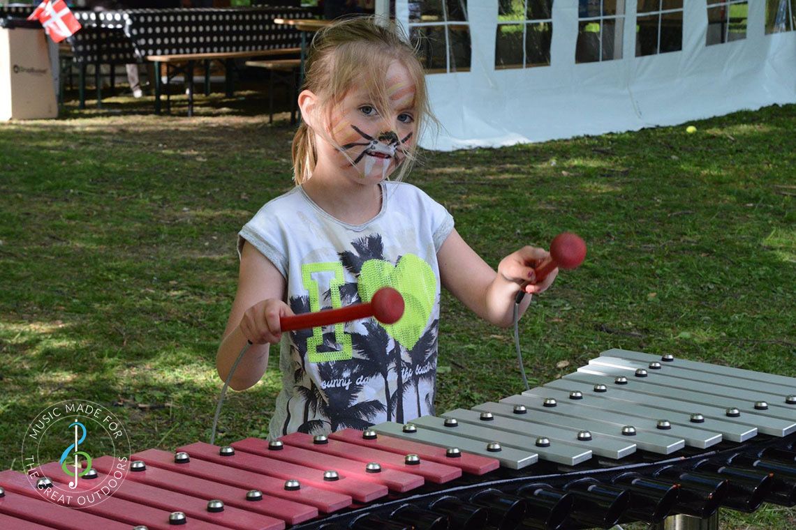 Young girl with her face painted playing a large outdoor xylophone in the park