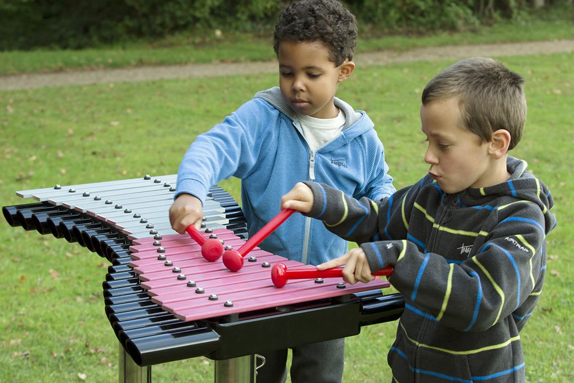 two little boys playing a large xylophone in a playground