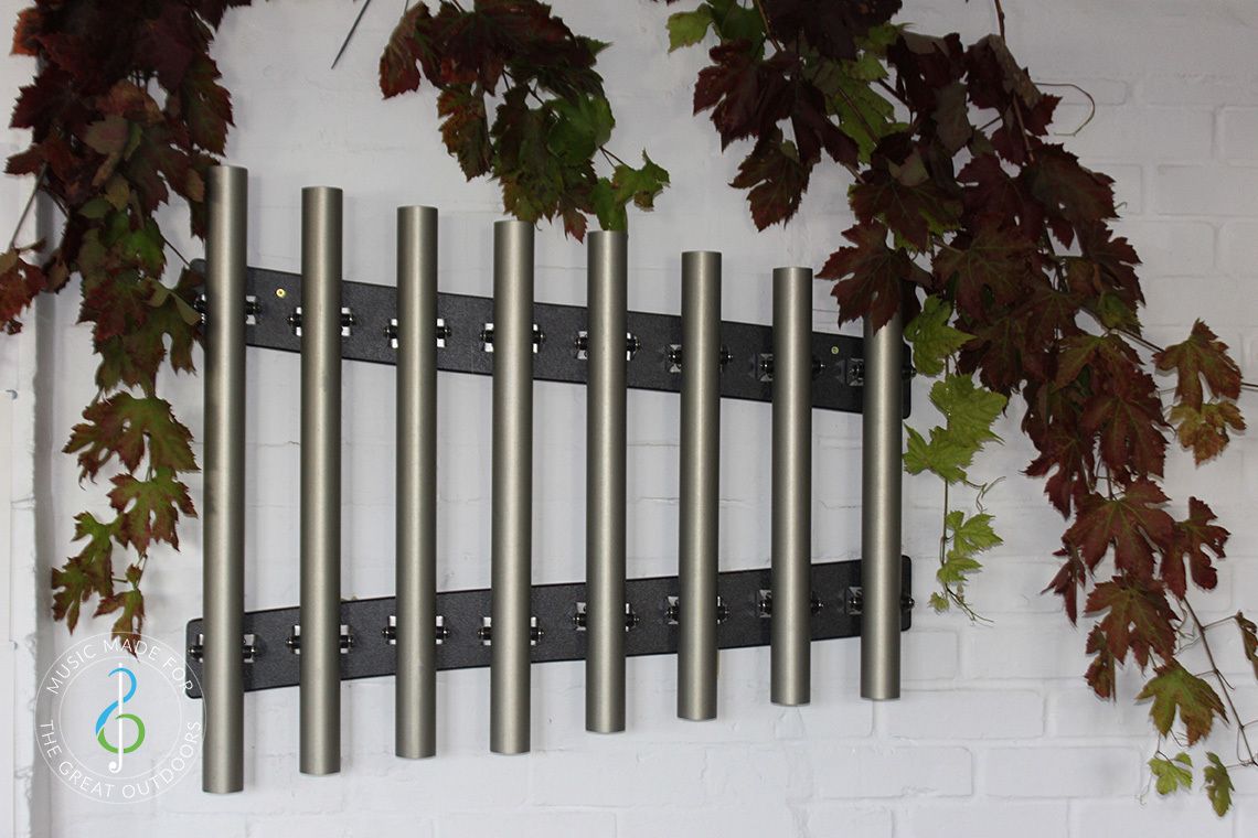 outdoor musical chimes mounted on a white wall covered in ivy