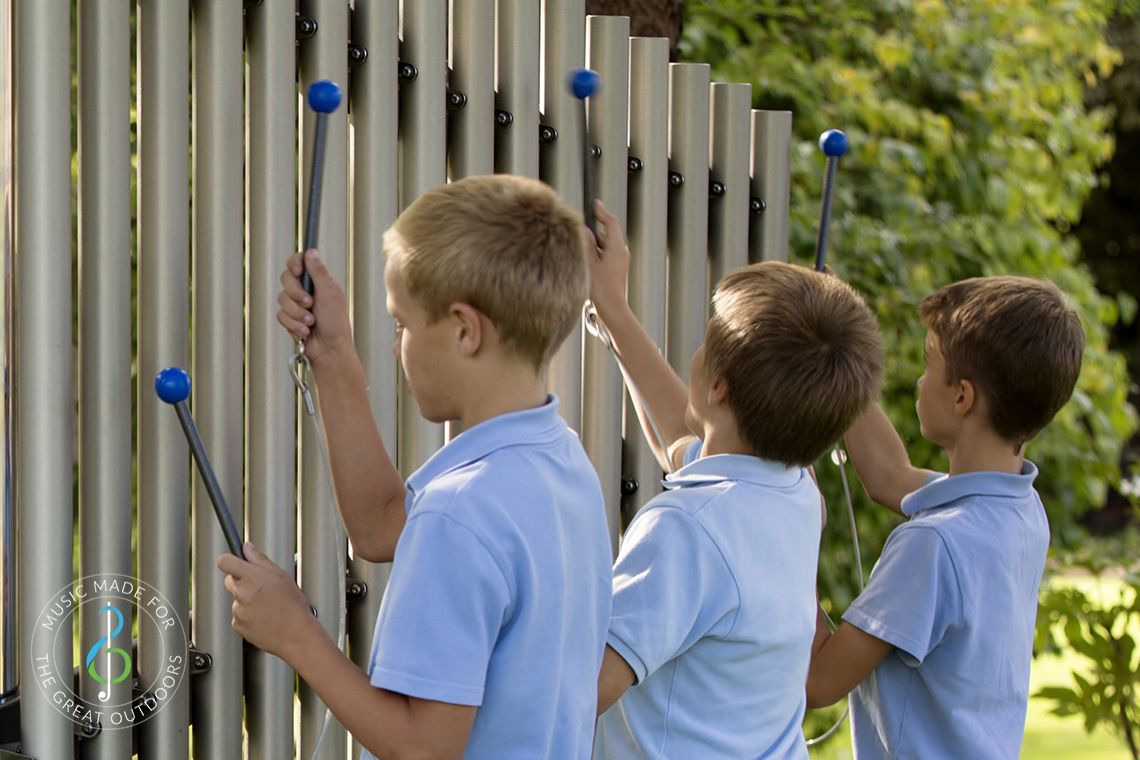 Close up image of three boys playing outdoor chimes in playground