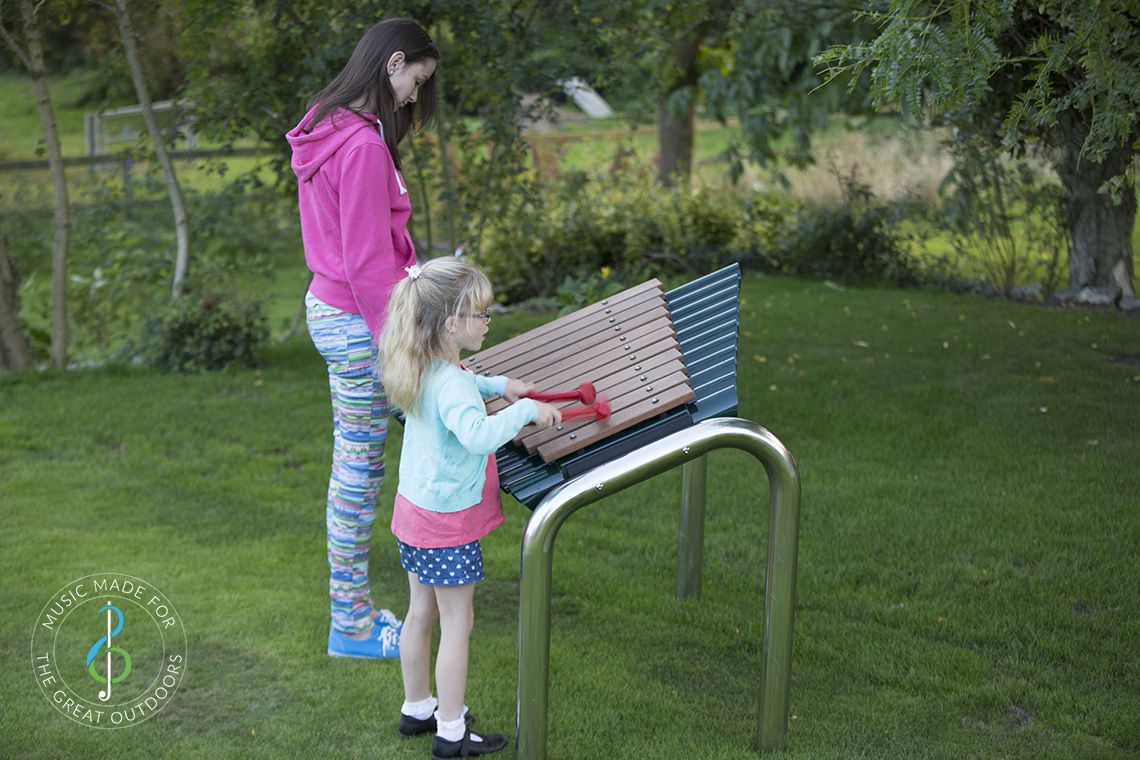 two girls in a park playing large outdoor marimba xylophone with wooden notes and stainless steel legs