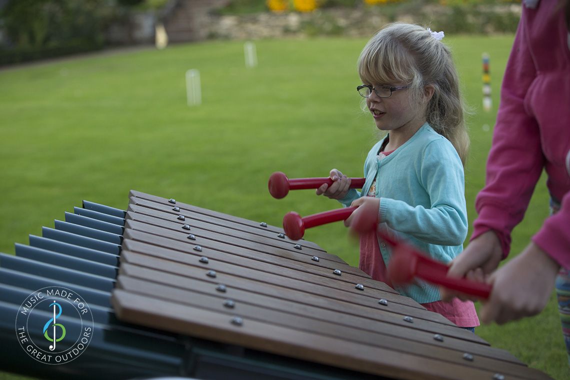 young girl wearing glasses playing on a large outdoor marimba xylophone in the park
