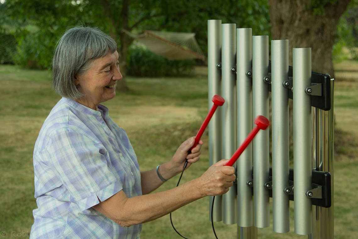 older lady smiling playing a set of outdoor musical chimes 