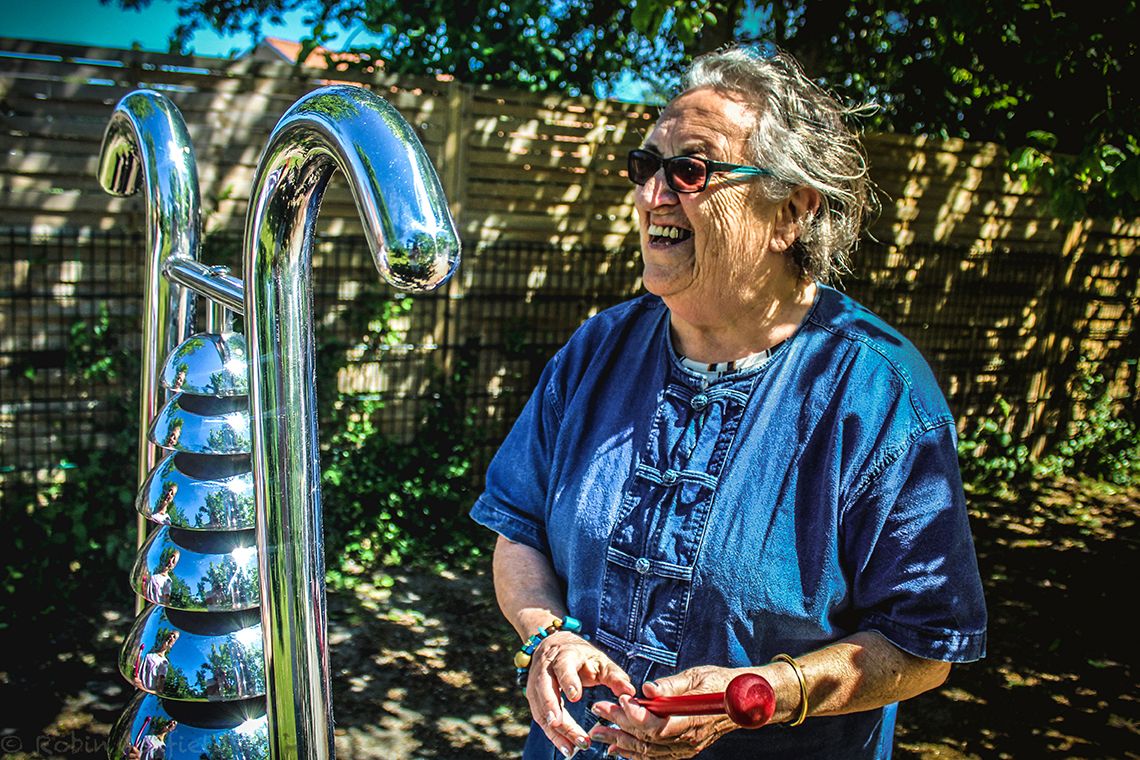 older lady laughing playing a large outdoor bell tree instrument
