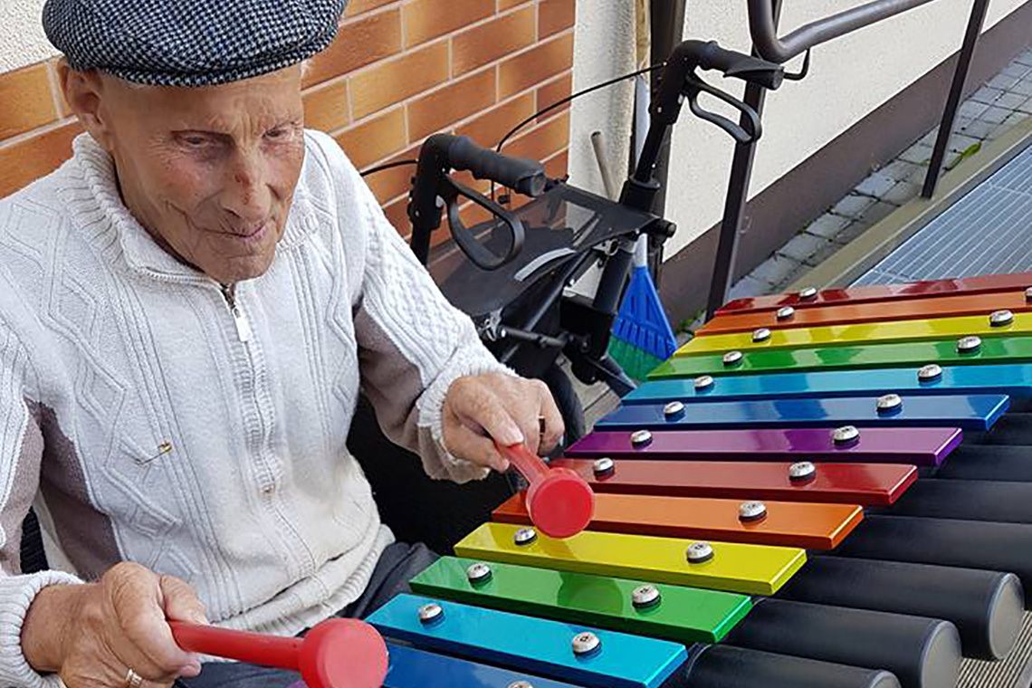 Older man in cap playing an outdoor xylophone wit rainbow notes