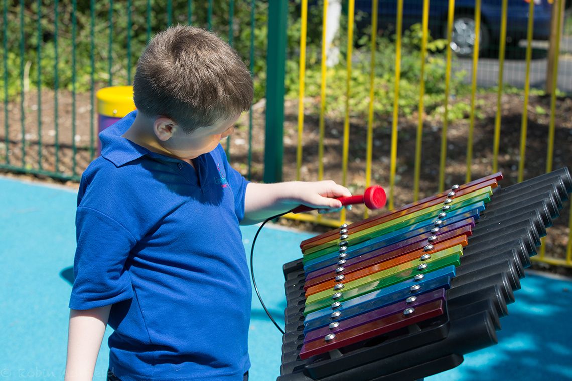 boys with special needs playing rainbow coloured chimes outdoors