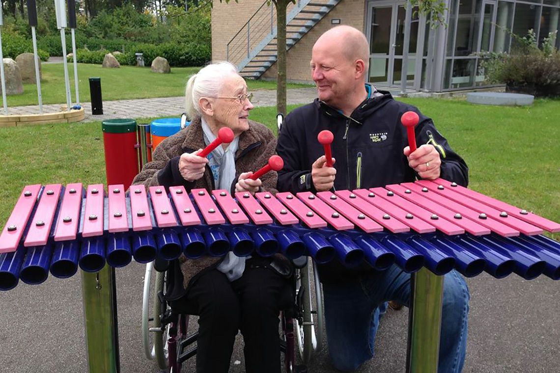 older lady and younger man playing an outdoor xylophone together in a care home garden