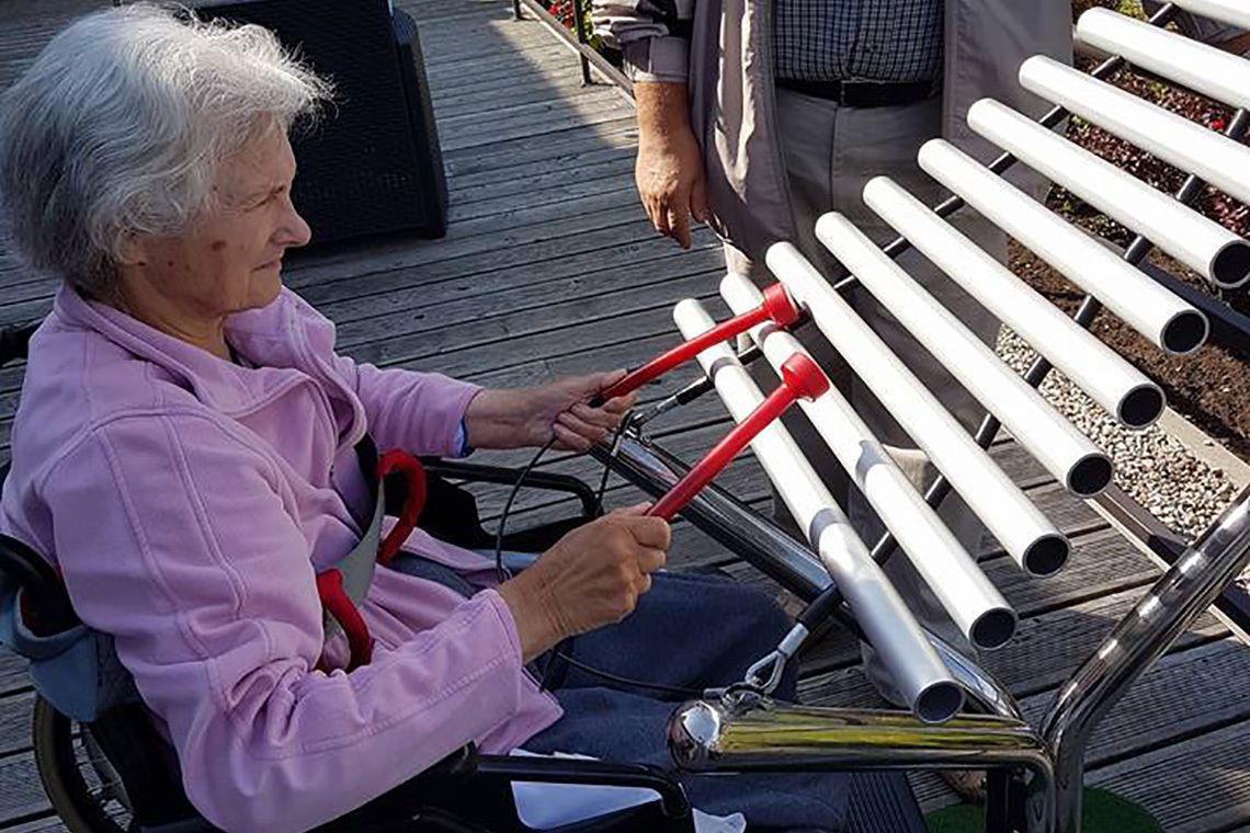 older lady in a wheelchair playing a large metallophone in a care home garden