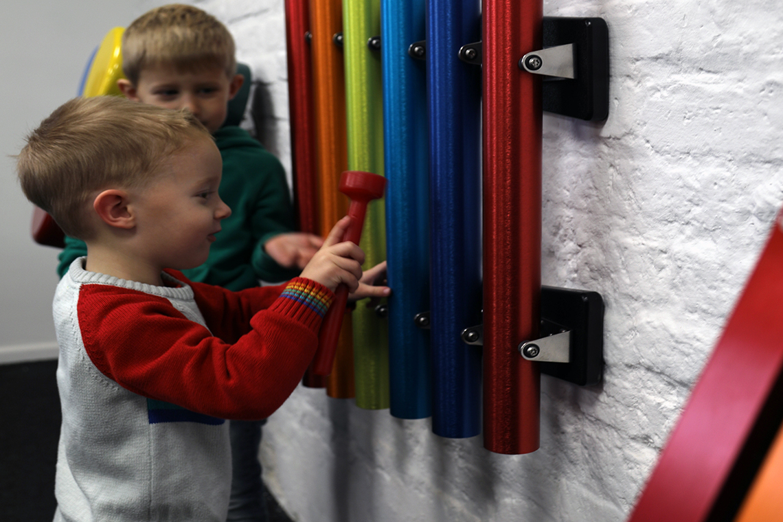a set of bright rainbow coloured pentatonic chimes for wall mounting in school playgrounds